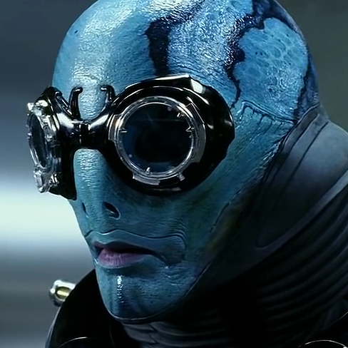 A blue-skinned person with darker blue squiggly stripes on their bald head and a very small nose, wearing black goggles