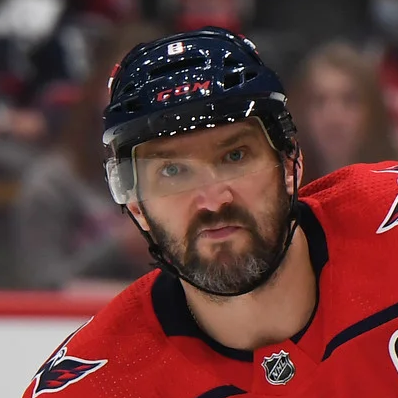 A light-skinned man with short brown-and-gray mustache and beard, wearing a black helmet and a red hockey uniform